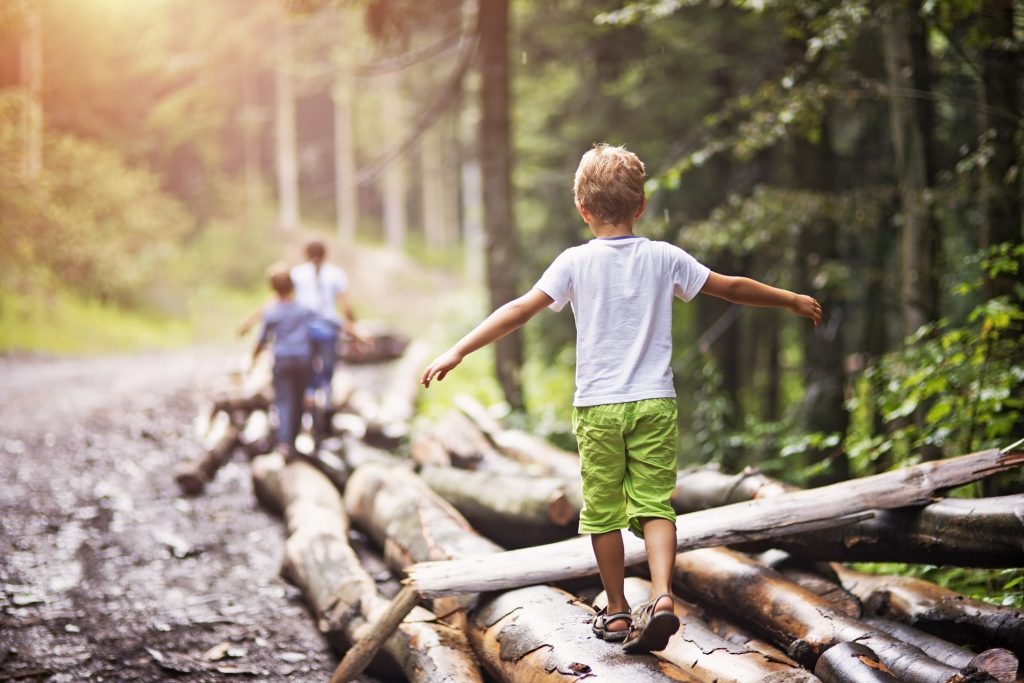 boys playing in the woods walking on a log