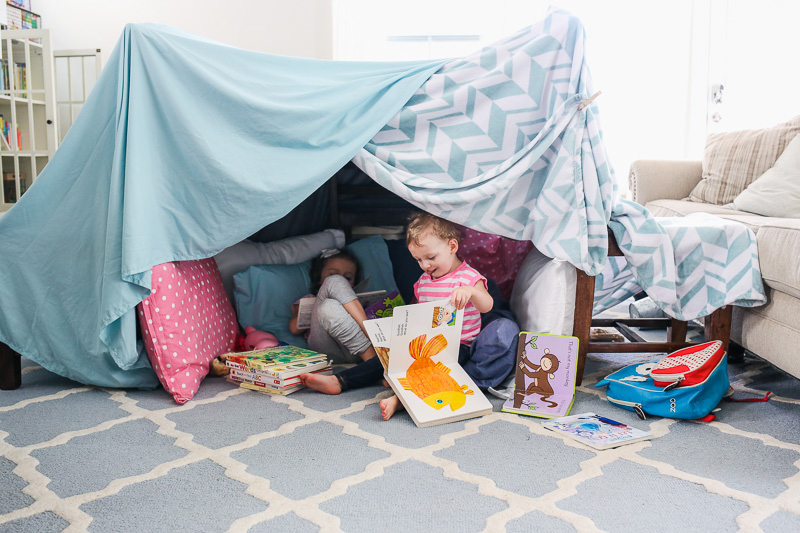 two girls playing in blue fort made of blankets and chairs